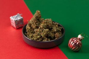 dry medical marijuana buds lie in a bowl next to a Christmas toy on a red and green background